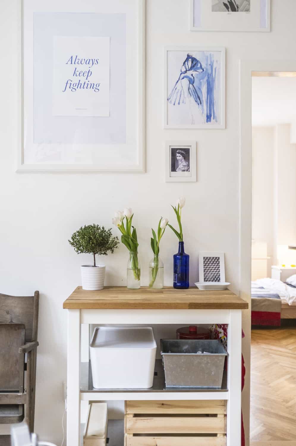 Shelf with bits and pieces up against the wall with artwork above it. 