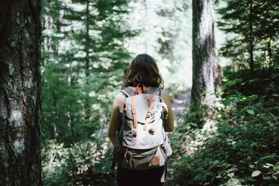 minimalist living - woman in sleeveless top and backpack surrounded by trees during daytime