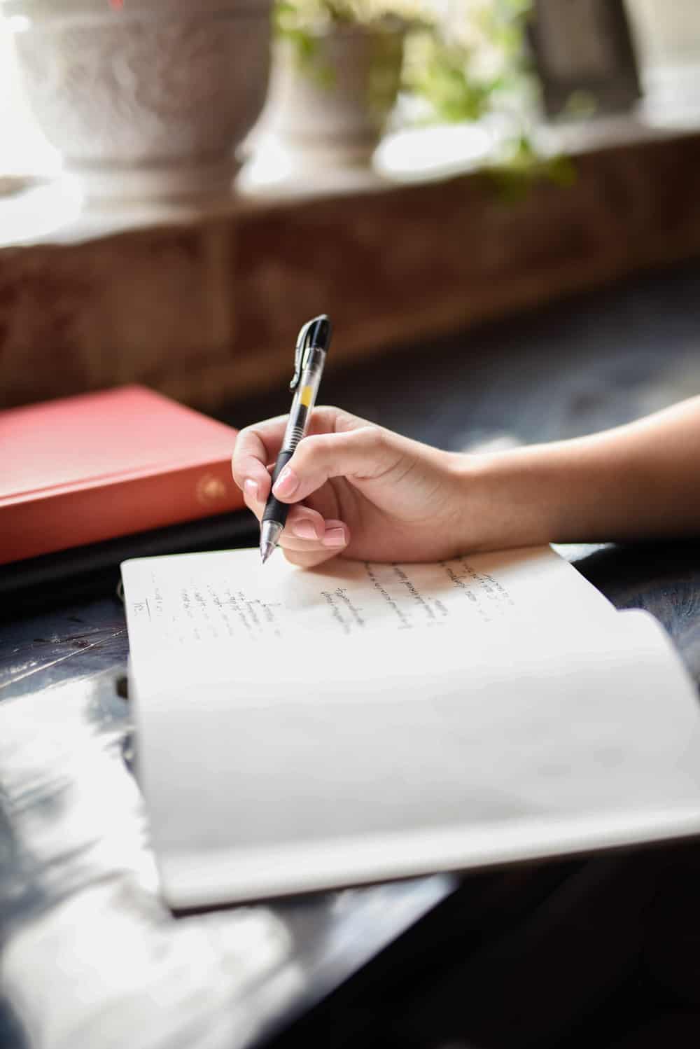 Journaling in cafe. Close up of hand holding a pen writing in notebook. 