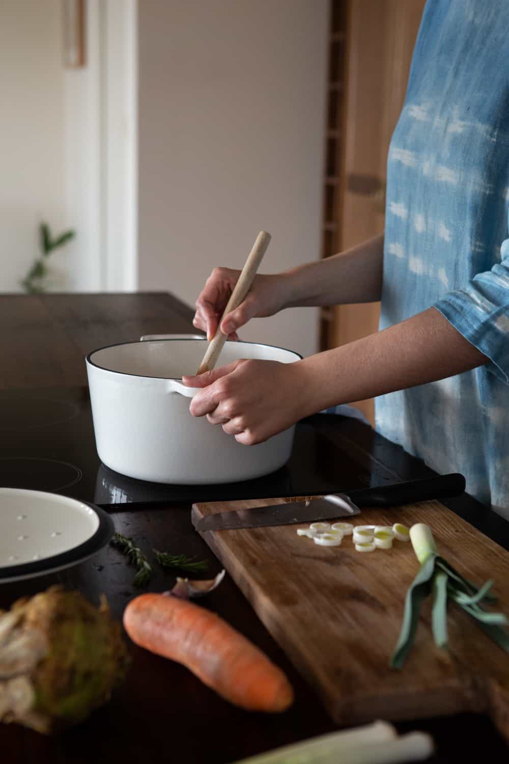 Woman stirring pot on stove with vegetables around.