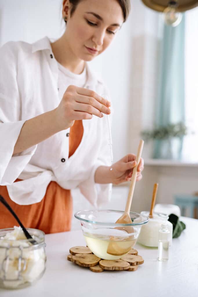 Woman using dropper to add liquid to melted wax in bowl.