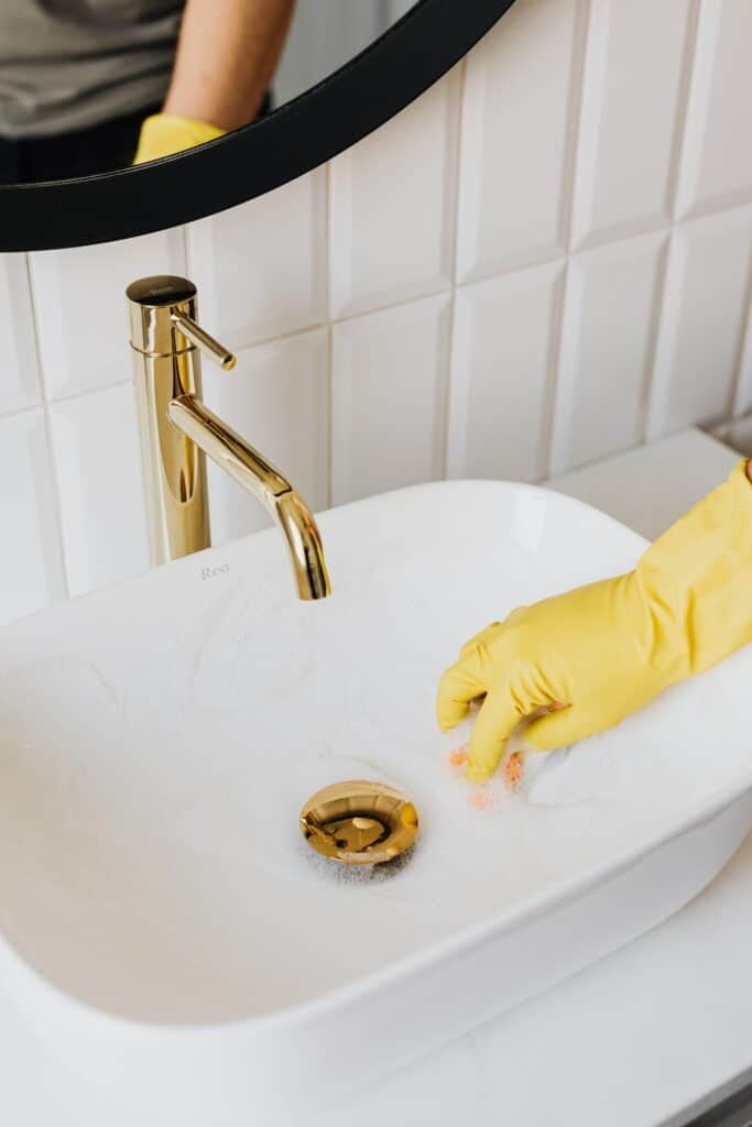 Cleaning bathroom sink with a yellow glove.