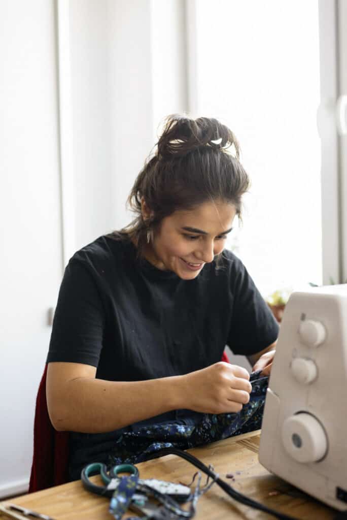 Woman smiling as she sews clothes on a sewing machine.